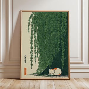 May include: A framed print featuring a sleeping cat under a weeping willow tree. The cat is white with orange markings. The tree has green leaves. The print has Japanese text and is in a wooden frame.