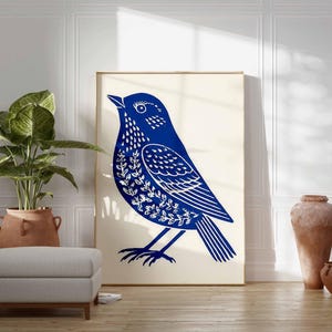 May include: A large framed print featuring a stylized blue bird illustration with white leaf-like details. The artwork is displayed against a neutral background, complemented by a potted plant, a gray ottoman, and terracotta vases, creating a serene, nature-inspired aesthetic.