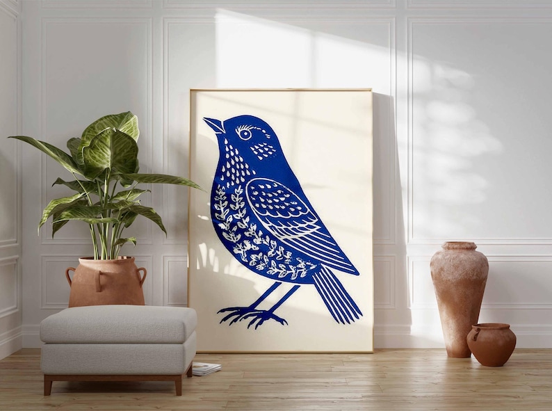 May include: A large framed print featuring a stylized blue bird illustration with white leaf-like details. The artwork is displayed against a neutral background, complemented by a potted plant, a gray ottoman, and terracotta vases, creating a serene, nature-inspired aesthetic.