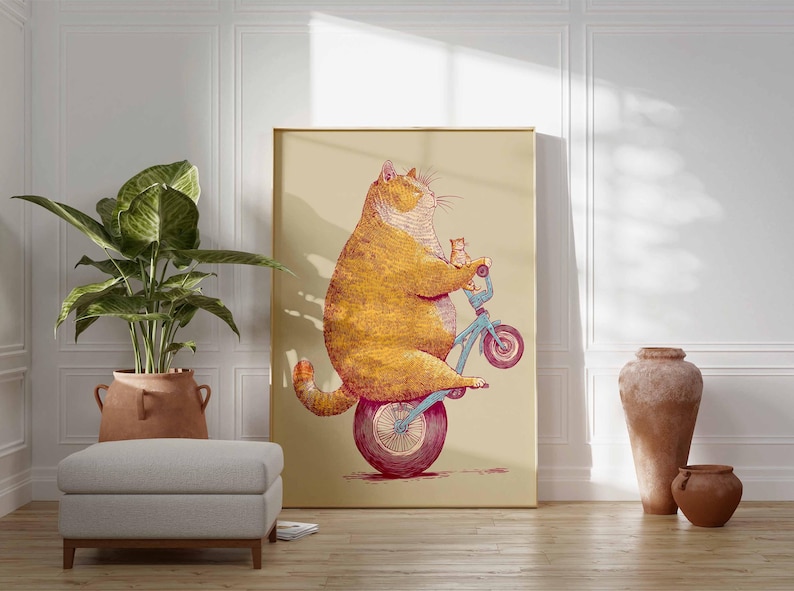 K&ouml;nnte beinhalten: Ein Kunstdruck zeigt eine Illustration einer orangefarbenen Katze auf einem blauen Fahrrad mit einem K&auml;tzchen. Das Kunstwerk ist vor einem beigen Hintergrund in Gold gerahmt. Der Raum umfasst eine Topfpflanze und Terrakotta-Vasen.