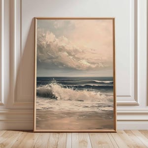 May include: A framed artwork depicts a seascape with a dynamic wave crashing onto a sandy beach. The sky is filled with soft, textured clouds, and the overall color palette is muted with shades of blue, beige, and white. The artwork is displayed in a wooden frame.