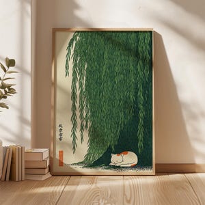 May include: A framed art print featuring a sleeping cat under a weeping willow tree. The artwork has a Japanese aesthetic, with a white and orange cat resting on the ground beneath the green foliage. The print includes Japanese text.