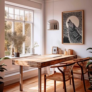 May include: A wooden desk with metal legs and two woven chairs in a bright room. A framed black and white print of a howling wolf hangs on the wall. A large window offers a view of trees and natural light.