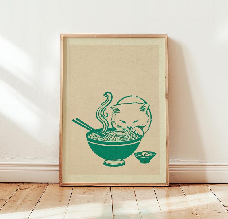 May include: A framed vertical art print on a light beige background featuring a dark green line drawing of a cat eating noodles from a bowl with chopsticks. A small side bowl is positioned to the right of the main bowl, completing the illustration.