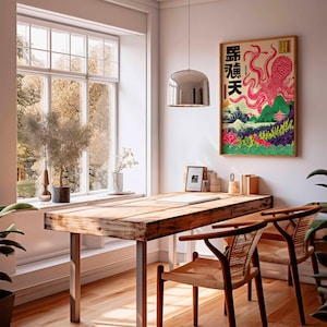 May include: A framed Japanese-style art print featuring a pink octopus with Japanese text. The artwork is set against a backdrop of mountains, a pagoda, and colorful foliage. The print hangs above a wooden desk with two woven chairs.