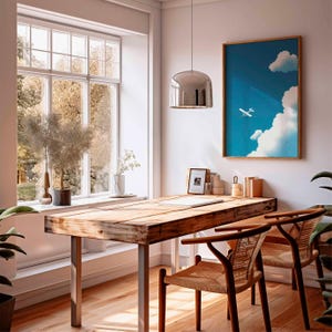 Peut inclure: Un bureau &agrave; domicile lumineux et a&eacute;r&eacute; avec un bureau en bois et deux chaises. Une &oelig;uvre d'art encadr&eacute;e d'un avion dans le ciel est accroch&eacute;e au mur. Une grande fen&ecirc;tre offre une vue sur les arbres. Une suspension argent&eacute;e est suspendue au-dessus du bureau.