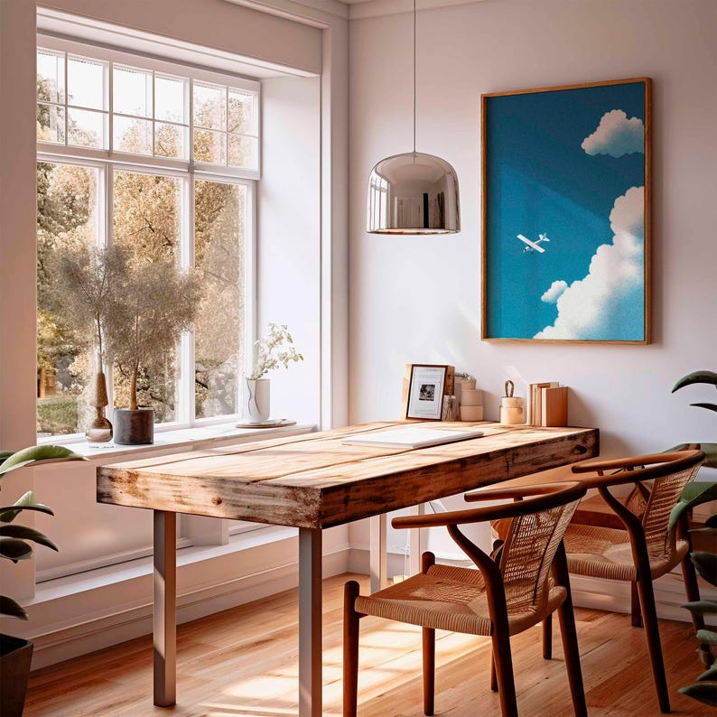 Peut inclure: Un bureau &agrave; domicile lumineux et a&eacute;r&eacute; avec un bureau en bois et deux chaises. Une &oelig;uvre d'art encadr&eacute;e d'un avion dans le ciel est accroch&eacute;e au mur. Une grande fen&ecirc;tre offre une vue sur les arbres. Une suspension argent&eacute;e est suspendue au-dessus du bureau.