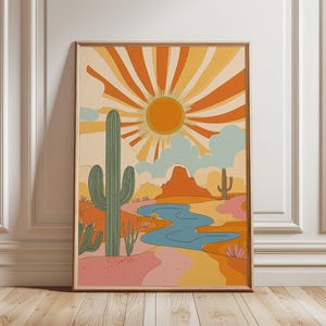 May include: A framed art print depicting a desert scene with a large sunburst in orange and yellow hues. The artwork showcases cacti, a blue river, and mountains, all rendered in a retro, vintage style.