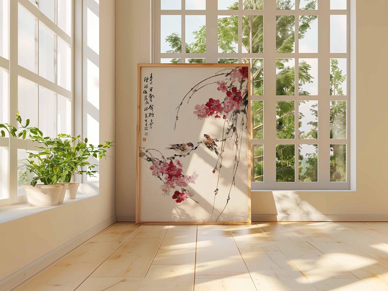 Peut inclure: Une &oelig;uvre d'art encadr&eacute;e repr&eacute;sentant une peinture de style asiatique. Elle montre deux oiseaux perch&eacute;s sur des branches fleuries roses et des baies rouges. Le fond est beige clair, et le cadre est marron clair. La pi&egrave;ce est &eacute;clair&eacute;e par une fen&ecirc;tre.