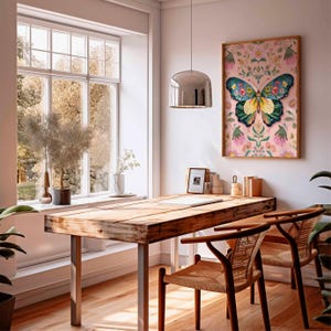 May include: A framed butterfly art print hangs above a wooden desk with metal legs. The butterfly has colorful wings against a pink floral background. Two woven chairs sit at the desk, near a large window.