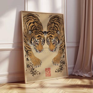 May include: Framed art print featuring two tigers facing each other. The tigers have orange and black stripes, with red eyes and a tan background. The print has a wooden frame and a red stamp in the lower right corner.