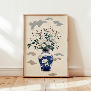 May include: A framed wall art print featuring a blue and white ceramic vase filled with white flowers and green leaves. The background is a light cream color decorated with stylized gray clouds. The frame is made of light-colored wood.