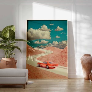 K&ouml;nnte beinhalten: Gerahmter Kunstdruck mit einem orangefarbenen Oldtimer, der auf einer kurvenreichen Stra&szlig;e durch eine rosa Landschaft unter blauem Himmel mit wei&szlig;en Wolken f&auml;hrt. Das Kunstwerk wird in einem Raum mit einer Pflanze, einem Hocker und dekorativen Vasen ausgestellt.