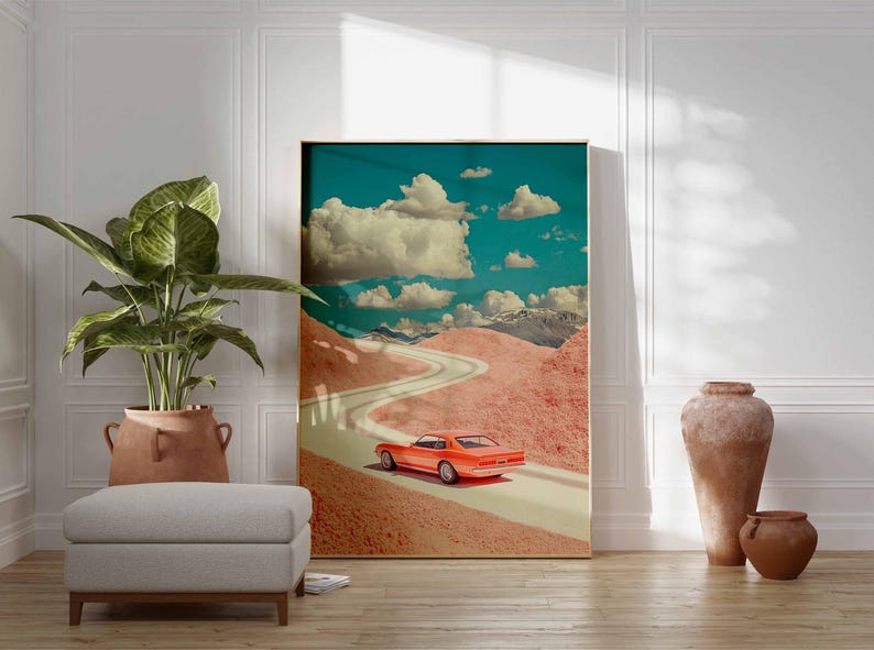 K&ouml;nnte beinhalten: Gerahmter Kunstdruck mit einem orangefarbenen Oldtimer, der auf einer kurvenreichen Stra&szlig;e durch eine rosa Landschaft unter blauem Himmel mit wei&szlig;en Wolken f&auml;hrt. Das Kunstwerk wird in einem Raum mit einer Pflanze, einem Hocker und dekorativen Vasen ausgestellt.