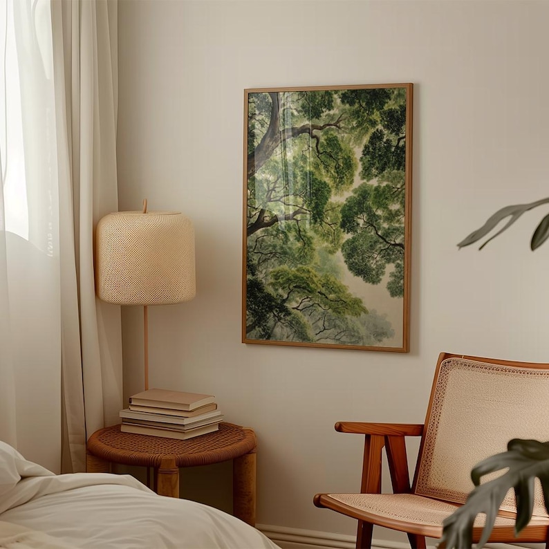 May include: A framed art print depicting a view of a tree canopy from below, with lush green leaves and branches. The artwork is in a wooden frame and hangs on a neutral-colored wall. A woven lamp and side table are in the foreground.