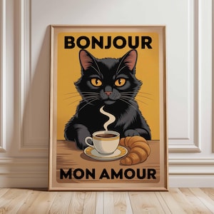 以下が含まれることがあります： 黒猫、コーヒーカップ、クロワッサンが描かれた額入りのアートプリント。「BONJOUR MON AMOUR」の文字。猫は黄色い目を持ち、背景はマスタードイエロー。木製のフレームに入っています。
