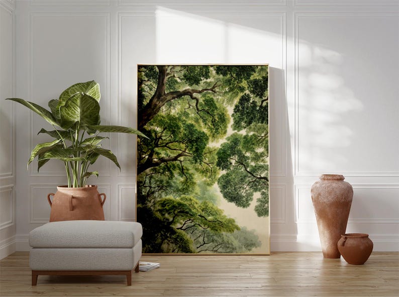 May include: A large framed art print of a tree canopy in shades of green and brown. The artwork is leaning against a white wall, next to a potted plant, a footstool, and two terracotta vases. The room has a natural, earthy aesthetic.
