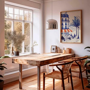 K&ouml;nnte beinhalten: Ein lichtdurchfluteter Raum mit einem Holztisch und zwei St&uuml;hlen. Ein gerahmter Druck eines Pariser Caf&eacute;s h&auml;ngt an der Wand. Ein gro&szlig;es Fenster bietet einen Blick auf B&auml;ume. Eine silberne Pendelleuchte h&auml;ngt &uuml;ber dem Schreibtisch.