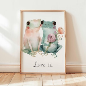 Peut inclure: Impression aquarelle encadrée de deux grenouilles, une rose et une bleue, s'embrassant. La grenouille bleue tient un bouquet de fleurs. L'inscription "Love is.." est en dessous. Le cadre est en bois clair.