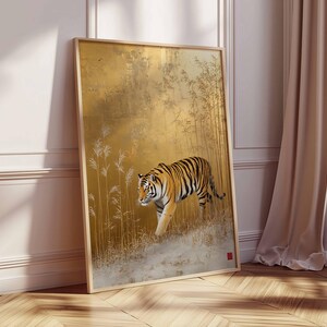 K&ouml;nnte beinhalten: Gerahmter Kunstdruck mit einer detaillierten Illustration eines Tigers, der durch eine goldfarbene Landschaft geht. Der Tiger hat orange und schwarze Streifen. Das Kunstwerk befindet sich in einem Holzrahmen und lehnt an einer wei&szlig;en Wand und einem Holzboden.