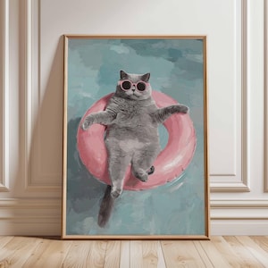Pode incluir: Impressão emoldurada de um gato cinza usando óculos de sol rosa, flutuando em um anel inflável rosa em uma piscina. O gato é o ponto focal, com uma pose relaxada. O fundo é azul claro, pintado para se assemelhar à água.