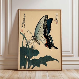 May include: Framed vintage-style print featuring a butterfly with light blue and black wings, perched on a plant with dark green leaves. The artwork has Japanese text and is set against a beige background.