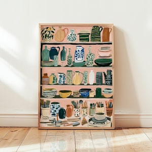 May include: A framed art print featuring a pink-toned shelving unit filled with various ceramic pottery, including pitchers, bowls, vases, and mugs in shades of blue, green, yellow, and brown, alongside containers holding assorted paintbrushes.