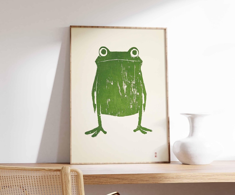 May include: A framed print of a green frog with a white background. The frog is stylized and has a simple design.