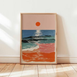 Puede incluir: Una impresión artística enmarcada que representa una puesta de sol sobre el océano. La obra de arte presenta un degradado de colores, incluyendo un cielo rosa, agua azul y olas naranjas. El sol es un círculo naranja brillante.