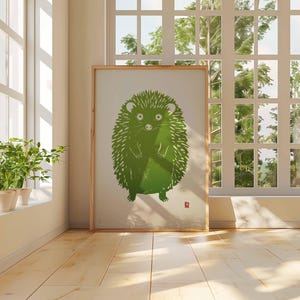 Pu&ograve; includere: Una stampa artistica incorniciata con un'illustrazione di un riccio verde. L'opera d'arte ha uno sfondo chiaro e una cornice in legno. L'immagine &egrave; esposta in una stanza con luce naturale, vicino a una finestra e piante in vaso. Il pavimento &egrave; in legno.