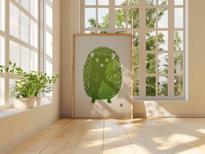 Pu&ograve; includere: Una stampa artistica incorniciata con un'illustrazione di un riccio verde. L'opera d'arte ha uno sfondo chiaro e una cornice in legno. L'immagine &egrave; esposta in una stanza con luce naturale, vicino a una finestra e piante in vaso. Il pavimento &egrave; in legno.