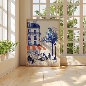 K&ouml;nnte beinhalten: Ein gerahmter Kunstdruck zeigt eine Pariser Caf&eacute;szene. Die Illustration zeigt Geb&auml;ude mit blauen und wei&szlig;en Details, eine rot-wei&szlig; gestreifte Markise und Personen, die an Tischen sitzen. Ein blauer Baum und eine Stra&szlig;enlaterne sind ebenfalls enthalten.