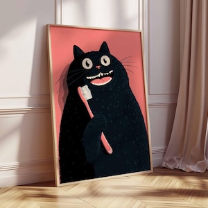 Op de afbeelding: Een ingelijste kunstdruk met een cartoon zwarte kat die een roze tandenborstel vasthoudt. De kat grijnst breed, tegen een roze achtergrond. De lijst heeft een lichte houtkleur. Het kunstwerk leunt tegen een muur.