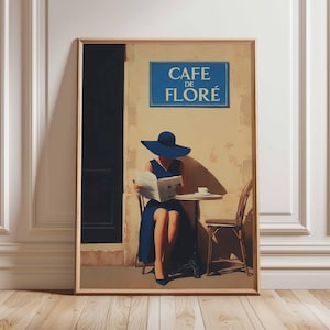May include: A framed art print depicts a woman in a blue dress and hat reading at a cafe table. The sign above reads "CAFE DE FLORE". The artwork has a vintage, painterly style, with a warm color palette and a wooden frame.