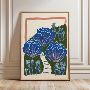 May include: A framed art print featuring a stylised illustration of three large blue cabbage heads with red veins, set against a dark green background. A light path winds between the cabbages, surrounded by small blue flowers and a peach-coloured border.