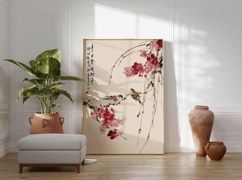 Peut inclure: Une &oelig;uvre d'art encadr&eacute;e repr&eacute;sentant une peinture de style asiatique avec des oiseaux et des fleurs roses. De la calligraphie est visible sur le c&ocirc;t&eacute; gauche. L'&oelig;uvre est expos&eacute;e dans une pi&egrave;ce avec une plante, un tabouret et des pots en terre cuite.