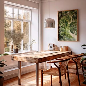 May include: A bright, airy home office with a large wooden desk and two woven chairs. A framed tree painting hangs on the wall. A large window offers a view of trees and natural light. A silver pendant light hangs above the desk.
