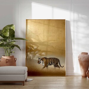 May include: A large framed artwork featuring a tiger walking through tall grass. The artwork has a gold background and a brown frame. A large potted plant, a footstool, and decorative vases are in front of the artwork.
