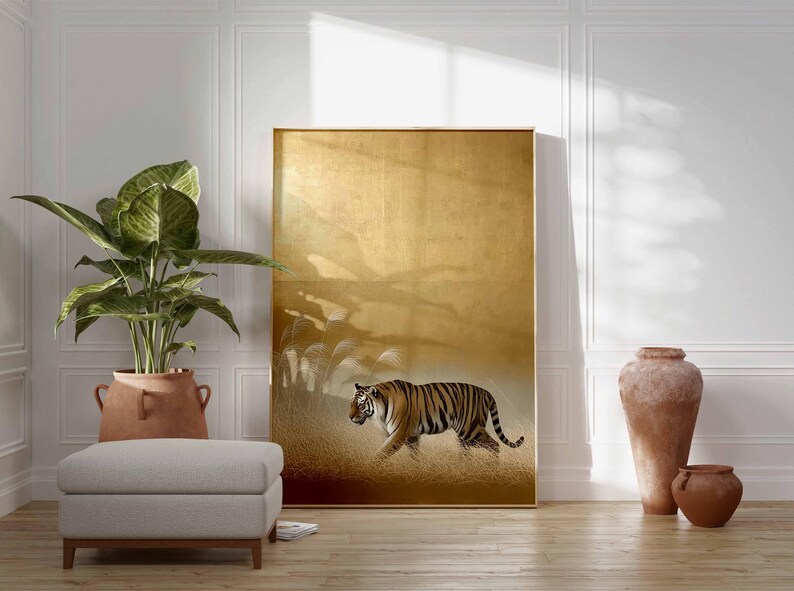 May include: A large framed artwork featuring a tiger walking through tall grass. The artwork has a gold background and a brown frame. A large potted plant, a footstool, and decorative vases are in front of the artwork.