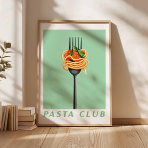 Op de afbeelding: Een ingelijste kunstafdruk met een zwarte vork met spaghetti, tomaat en basilicum. De pasta is kunstzinnig gerangschikt op de vork tegen een lichtgroene achtergrond. De tekst "PASTA CLUB" staat onderaan.