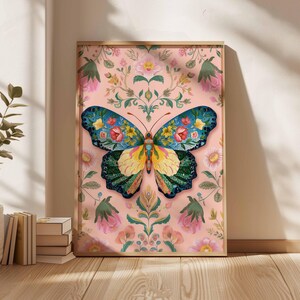 May include: A framed art print featuring a colorful butterfly illustration. The butterfly has blue, yellow, and green wings adorned with floral patterns. The background is a pink floral design, and the frame is a light brown color.