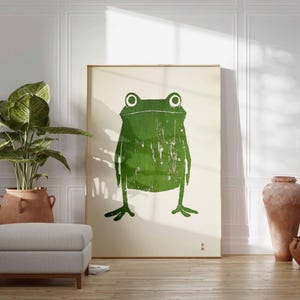 May include: A framed print of a green frog with a textured, distressed look. The frog is centered on a white background.