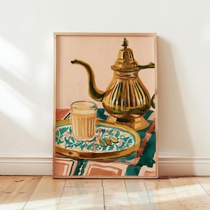 Op de afbeelding: Een ingelijste kunstdruk met een gouden metalen theepot en een glas lichtbruine thee op een ovaal dienblad met patronen. Het dienblad heeft een blauwgroen en wit bloemmotief met groene kardemompeulen tegen een achtergrond van geometrische vormen.