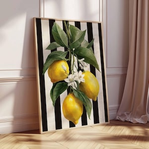 May include: A framed art print featuring a watercolor illustration of lemons on a branch with green leaves and white blossoms. The background has black and white vertical stripes. The artwork is displayed against a white wall and wooden floor.
