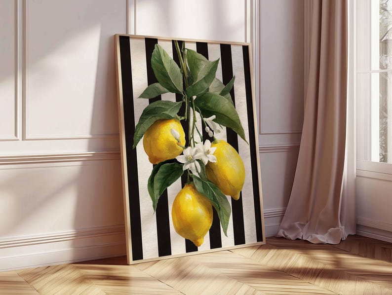 May include: A framed art print featuring a watercolor illustration of lemons on a branch with green leaves and white blossoms. The background has black and white vertical stripes. The artwork is displayed against a white wall and wooden floor.