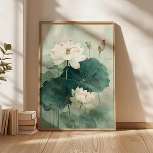 Puede incluir: Una impresi&oacute;n art&iacute;stica enmarcada que presenta una pintura de acuarela de flores de loto blancas con hojas verdes. La obra de arte tiene una paleta de colores suaves y apagados con un fondo verde claro. El marco es de color madera clara.