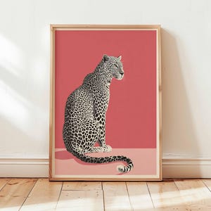 以下が含まれることがあります： ヒョウのイラストが描かれた額入りのアートプリント。ヒョウは白黒で斑点模様で描かれ、コーラルピンクの背景に配置されています。アートワークは、インテリア装飾に最適な、明るい茶色の木製フレームに収められています。