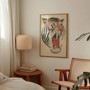 May include: A framed art print featuring a tiger's head with an open mouth, showcasing sharp teeth and a red interior. The tiger has orange and black stripes, set against a beige background. The frame is a light brown color.