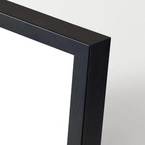 May include: Close-up of a black picture frame corner. The frame is made of wood and has a matte finish. The corner is a clean 90-degree angle, with a white background.