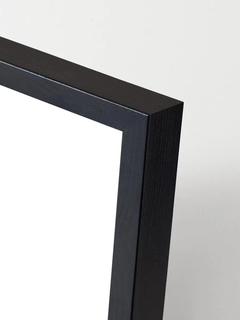 May include: Close-up of a black picture frame corner. The frame is made of wood and has a matte finish. The corner is a clean 90-degree angle, with a white background.
